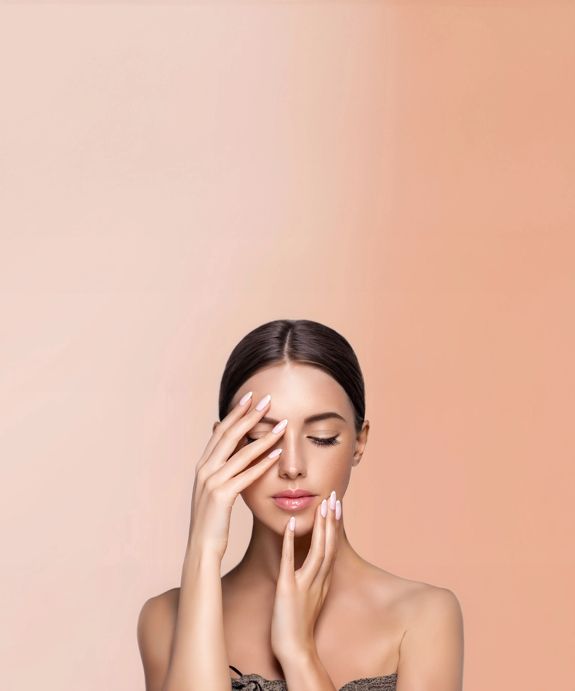 Nahaufnahme eines weiblichen Gesichts mit geschlossenen Augen und glänzenden Lippen. Die Frau präsentiert ihre perfekt manikürten, rosafarben lackierten Fingernägel vor ihrem Gesicht. Der Hintergrund ist in einem sanften Nude-Ton gehalten und vermittelt eine elegante, ästhetische Atmosphäre.